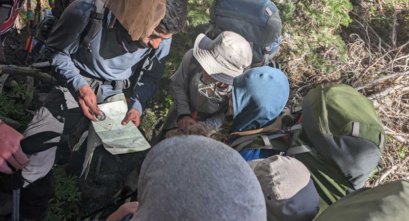 A group of people wearing stand in a circle and examine a map.